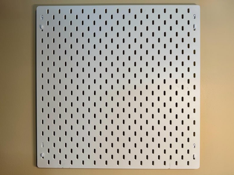 Peut inclure: Un panneau perfor&eacute; carr&eacute; de couleur blanche pr&eacute;sentant une grille uniforme de fentes verticales en forme de rectangle arrondi. Le panneau comporte quatre petits trous de fixation situ&eacute;s pr&egrave;s de chaque coin pour le montage mural.