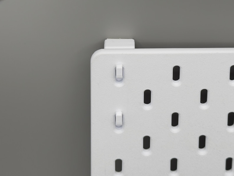 Peut inclure: Un panneau perfor&eacute; rectangulaire blanc dot&eacute; d'une grille de trous ovales verticaux r&eacute;guli&egrave;rement espac&eacute;s. Le panneau pr&eacute;sente une finition mate lisse et comprend un petit support de montage blanc fix&eacute; sur le bord sup&eacute;rieur.