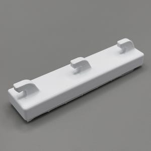 Peut inclure: Une bande de crochet murale rectangulaire en plastique blanc dot&eacute;e de trois crochets uniform&eacute;ment espac&eacute;s et incurv&eacute;s vers le haut. La base est un bloc solide et allong&eacute; avec une finition lisse, con&ccedil;ue pour &ecirc;tre fix&eacute;e sur une surface plane.