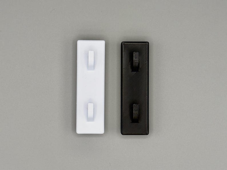 Peut inclure: Deux organisateurs muraux rectangulaires, l'un en blanc uni et l'autre en noir uni. Chaque organisateur comporte deux petits crochets saillants align&eacute;s verticalement sur une plaque de base plate et textur&eacute;e, con&ccedil;us pour suspendre des objets.