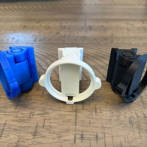 May include: Three 3D printed camera mounts in blue, white, and black. The mounts are designed to attach to a camera and allow it to be mounted in different positions.