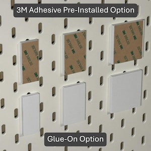May include: White pegboard accessories with 3M adhesive pre-installed and glue-on options. The image shows rectangular and square pieces, some with brown adhesive tape. Text at the top reads "3M Adhesive Pre-Installed Option" and at the bottom "Glue-On Option."