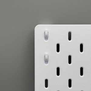 Peut inclure: Un panneau perfor&eacute; blanc pr&eacute;sentant une grille de fentes ovales verticales r&eacute;guli&egrave;rement espac&eacute;es. Deux petits crochets en plastique blanc sont ins&eacute;r&eacute;s dans les fentes sup&eacute;rieures gauches du panneau, qui poss&egrave;de une finition mate lisse.