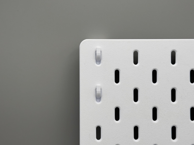 Peut inclure: Un panneau perfor&eacute; blanc pr&eacute;sentant une grille de fentes ovales verticales r&eacute;guli&egrave;rement espac&eacute;es. Deux petits crochets en plastique blanc sont ins&eacute;r&eacute;s dans les fentes sup&eacute;rieures gauches du panneau, qui poss&egrave;de une finition mate lisse.