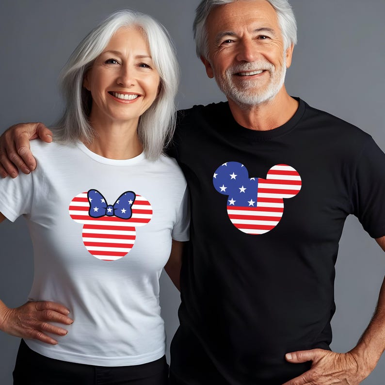 May include: A couple in matching t-shirts featuring a patriotic Mickey Mouse design. The woman's white t-shirt has a Minnie Mouse design with a red and white striped head and a blue bow. The man's black t-shirt has a Mickey Mouse head design.