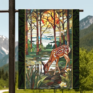 May include: A stained glass style garden flag featuring a deer in a forest setting. The deer is brown and white and is drinking from a stream. The background is a forest with trees and a sunset.