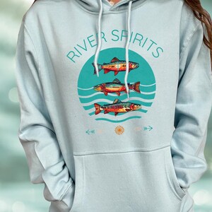 May include: Light blue hoodie with a front graphic. The graphic features three colorful fish above wavy lines, inside a teal circle. The words "RIVER SPIRITS" are arched above the circle. Arrows and a sun graphic are below the circle.