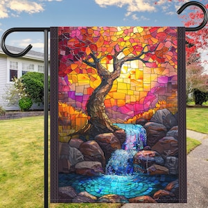 May include: A stained glass style garden flag featuring a tree with colorful leaves and a waterfall flowing over rocks. The background is a sunset with shades of orange, yellow, and pink.