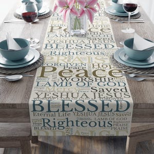 May include: A beige table runner with a white background and a pattern of words in brown and blue. The words include "Peace", "Worship", "Lamb of God", "Blessed", "Righteous", "Yeshua", "Jesus", "Saved", "Forgiven", "Faith", "Hope", "Mercy", and "Praise".