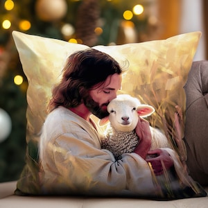 May include: A throw pillow with a painting of Jesus holding a lamb in his arms. The painting is done in a soft, warm color palette with a golden glow around Jesus's head. The lamb is white and fluffy, and Jesus is looking down at it with a gentle expression.