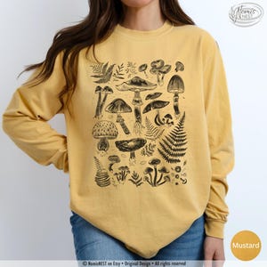 A mustard colored Comfort Colors long sleeve mushroom graphic t-shirt featuring illustrated botanical mushrooms which is perfect for granola girls, mushroom fans, those seeking a forestcore aesthetic, or nature lovers.