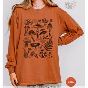A yam colored Comfort Colors long sleeve mushroom graphic t-shirt featuring illustrated botanical mushrooms which is perfect for granola girls, mushroom fans, those seeking a forestcore aesthetic, or nature lovers.