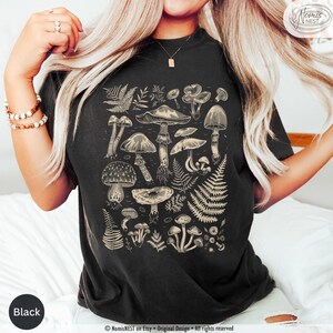 A black colored Comfort Colors graphic t-shirt featuring a monochromatic array of illustrated botanical mushrooms. It’s a perfect gift for nature lovers, mushroom foragers, granola girls, and forest wanderers.