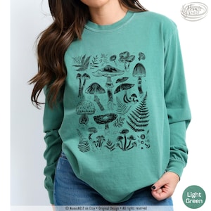 A light green colored Comfort Colors long sleeve mushroom graphic t-shirt featuring illustrated botanical mushrooms which is perfect for granola girls, mushroom fans, those seeking a forestcore aesthetic, or nature lovers.