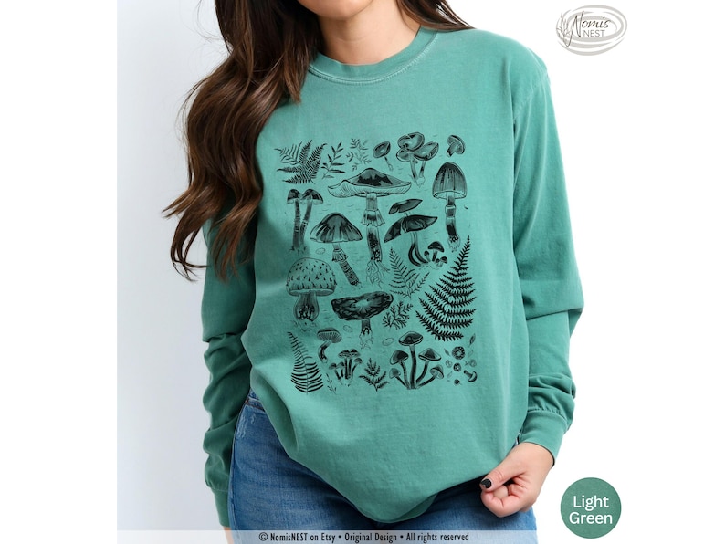 A light green colored Comfort Colors long sleeve mushroom graphic t-shirt featuring illustrated botanical mushrooms which is perfect for granola girls, mushroom fans, those seeking a forestcore aesthetic, or nature lovers.
