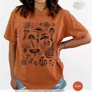 A yam colored Comfort Colors graphic t-shirt featuring a monochromatic array of illustrated botanical mushrooms. It’s a perfect gift for nature lovers, mushroom foragers, granola girls, and forest wanderers.
