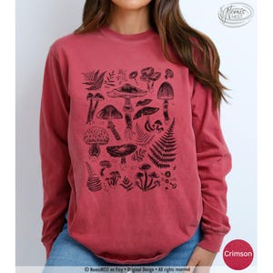 A crimson colored Comfort Colors long sleeve mushroom graphic t-shirt featuring illustrated botanical mushrooms which is perfect for granola girls, mushroom fans, those seeking a forestcore aesthetic, or nature lovers.