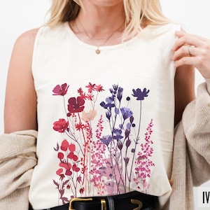 May include: Ivory-colored tank top featuring a floral design in shades of red, purple, and pink. The sleeveless shirt has a round neckline and a graphic of various flowers. The word "IVORY" is printed at the bottom right.