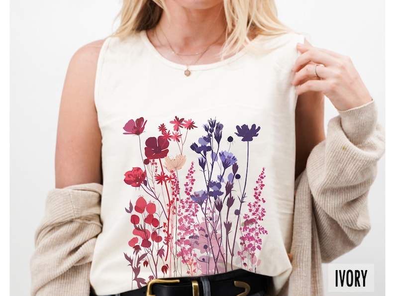 May include: Ivory-colored tank top featuring a floral design in shades of red, purple, and pink. The sleeveless shirt has a round neckline and a graphic of various flowers. The word "IVORY" is printed at the bottom right.