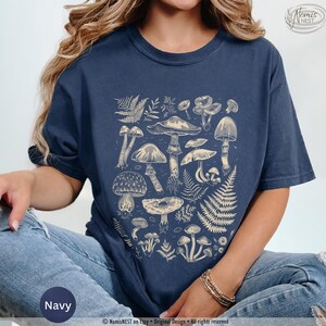A navy colored Comfort Colors graphic t-shirt featuring a monochromatic array of illustrated botanical mushrooms. It’s a perfect gift for nature lovers, mushroom foragers, granola girls, and forest wanderers.