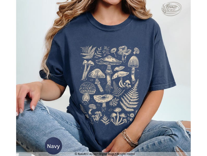 A navy colored Comfort Colors graphic t-shirt featuring a monochromatic array of illustrated botanical mushrooms. It’s a perfect gift for nature lovers, mushroom foragers, granola girls, and forest wanderers.