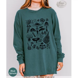 A blue spruce colored Comfort Colors long sleeve mushroom graphic t-shirt featuring illustrated botanical mushrooms which is perfect for granola girls, mushroom fans, those seeking a forestcore aesthetic, or nature lovers.