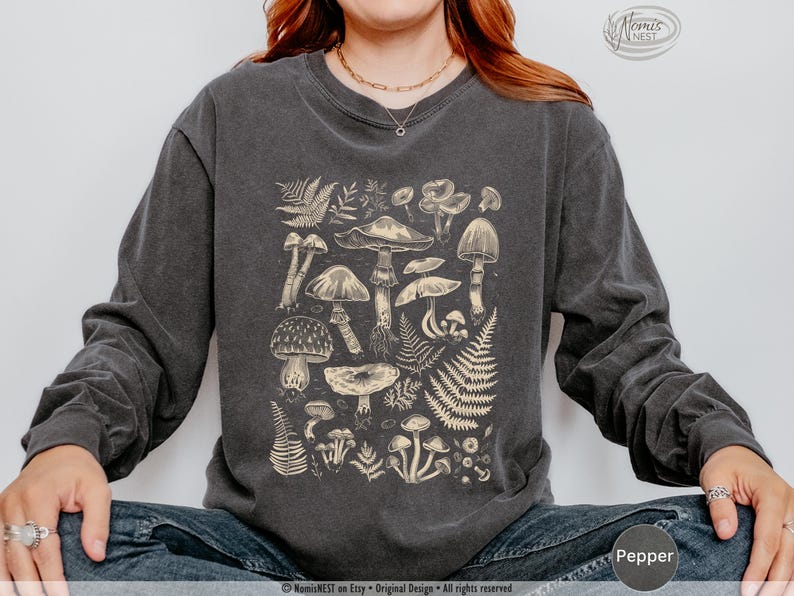 A pepper colored Comfort Colors long sleeve mushroom graphic t-shirt featuring illustrated botanical mushrooms which is perfect for granola girls, mushroom fans, those seeking a forestcore aesthetic, or nature lovers.
