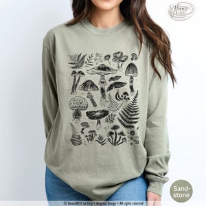 A sandstone colored Comfort Colors long sleeve mushroom graphic t-shirt featuring illustrated botanical mushrooms which is perfect for granola girls, mushroom fans, those seeking a forestcore aesthetic, or nature lovers.