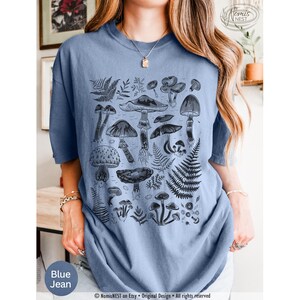 A blue jean Comfort Colors graphic t-shirt featuring a monochromatic array of illustrated botanical mushrooms. It’s a perfect gift for nature lovers, mushroom foragers, granola girls, and forest wanderers.