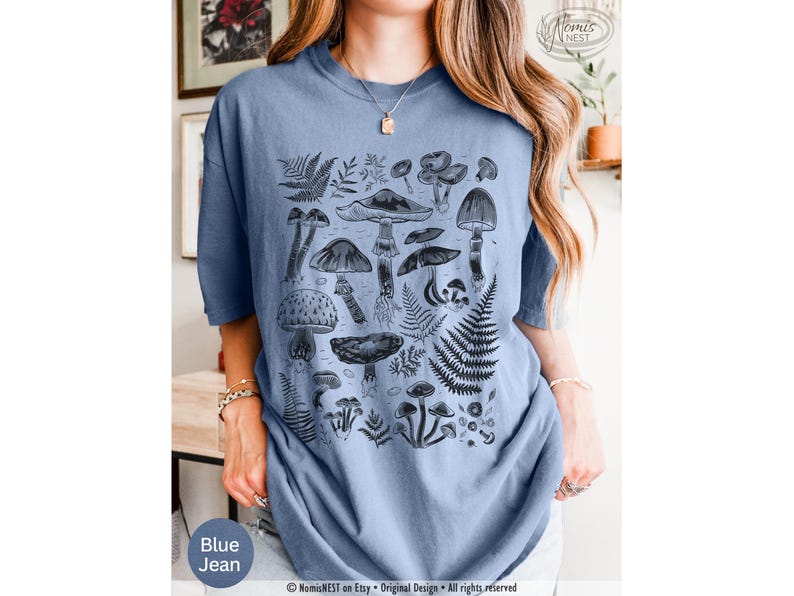 A blue jean Comfort Colors graphic t-shirt featuring a monochromatic array of illustrated botanical mushrooms. It’s a perfect gift for nature lovers, mushroom foragers, granola girls, and forest wanderers.