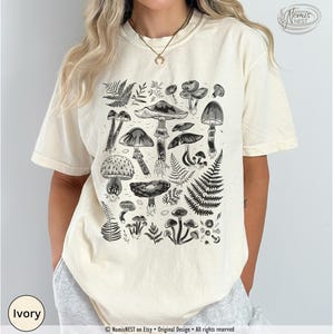 An ivory colored Comfort Colors graphic t-shirt featuring a monochromatic array of illustrated botanical mushrooms. It’s a perfect gift for nature lovers, mushroom foragers, granola girls, and forest wanderers.