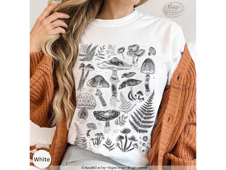 A white colored Comfort Colors graphic t-shirt featuring a monochromatic array of illustrated botanical mushrooms. It’s a perfect gift for nature lovers, mushroom foragers, granola girls, and forest wanderers.