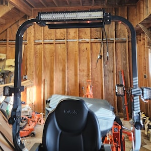 May include: Black tractor roll bar with LED light bar and side lights. The tractor has a black seat with the Kubota logo. The background is a wooden wall.