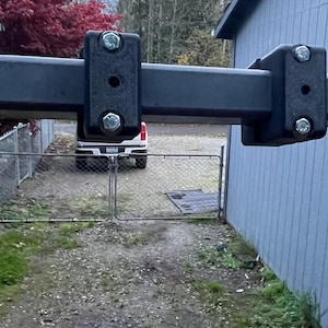 May include: A black metal frame with two black plastic brackets attached to it. The frame is mounted to a wall and appears to be part of a swing set.