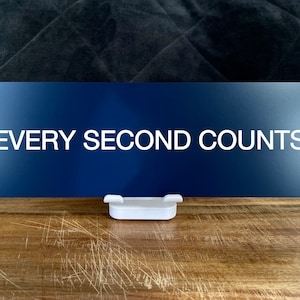Könnte beinhalten: Ein blaues Schild mit weißem Text, auf dem "EVERY SECOND COUNTS" steht, auf einem weißen Ständer.