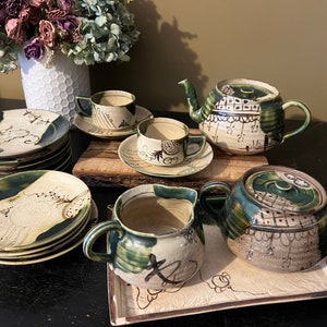 May include: A vintage Japanese tea set with a green and brown floral design. The set includes a teapot, creamer, sugar bowl, cups, and saucers.