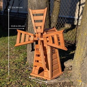 May include: A wooden windmill garden ornament with a natural brown finish. It features four slatted blades and a central tower structure. Dimensions are 44 cm in height, 35 cm in blade width, and 18 cm in base width as indicated in the image.