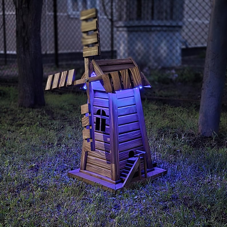 May include: A wooden windmill garden ornament featuring a dark brown stained finish, a rotating blade assembly, a small staircase leading to a side entrance, and integrated blue LED lighting that illuminates the structure from within.