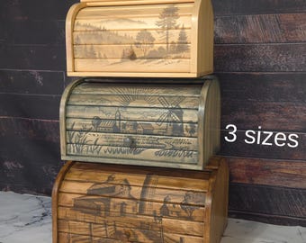 May include: Three wooden bread bins with different designs. The top bin is light brown with a landscape scene, the middle bin is grey with a windmill scene, and the bottom bin is dark brown with a farmhouse scene. The text "3 sizes" is visible in the image.