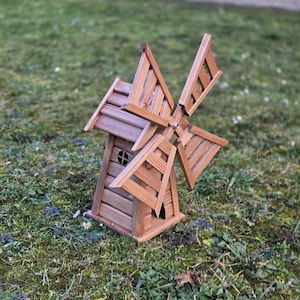 May include: A brown wooden windmill model featuring a slatted main structure with a small circular window and four rotating blades attached to the front. The windmill is constructed from horizontal planks and has a pointed roof design.