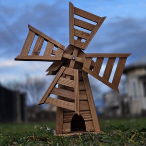 May include: A wooden windmill garden ornament featuring a natural brown finish with visible wood grain. The structure has a tapered base with an arched opening and four large, slatted blades attached to a central hub with a visible metal bolt.