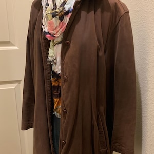 May include: A brown leather jacket with a button closure and a colorful scarf. The jacket has a quilted lining and a long, fitted style.