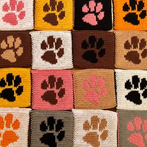 May include: A collection of 16 knitted squares featuring paw prints in various colors, including pink, brown, black, orange, and yellow. The squares are arranged in a grid pattern.