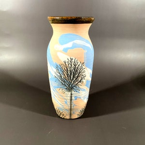 May include: A ceramic vase with a light blue, pink, and white marbled design. A black silhouette of a tree is painted on the front of the vase.