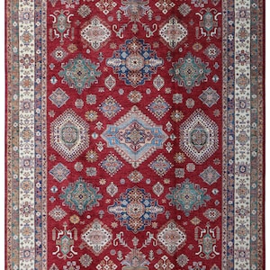 Könnte beinhalten: Ein roter Orientteppich mit einem aufwendigen geometrischen Muster. Das zentrale Feld des Teppichs ist rot und mit geometrischen Formen in Blau, Türkis und Weiß verziert. Ein cremefarbener Rand umrahmt das Design und setzt Kontraste.