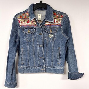 May include: A blue denim jacket with a floral embroidered yoke. The jacket has a button closure and two front pockets.