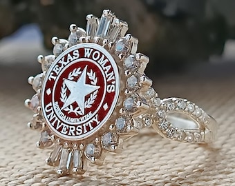 May include: A silver ring with a red and white Texas Woman's University logo. The ring is set with clear stones and has a band that is decorated with small stones.