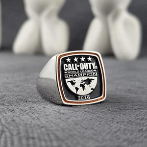 May include: A silver ring with a rectangular face featuring the text "Call of Duty World League Champion" and the year "2016". The face has a black background with a world map graphic and four stars.