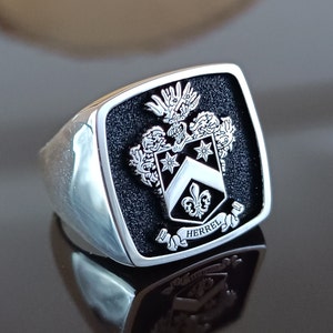 May include: A silver signet ring with a black enamel square top featuring a silver coat of arms with the text "Herrel".