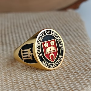 以下が含まれることがあります： 黒と赤のエナメルデザインの金の指輪。指輪にはレスター大学の紋章と「University of Leicester Archaeology」の文字が刻まれています。